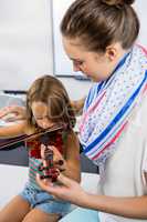 Teacher assisting girl to play violin whiteboard in classroom