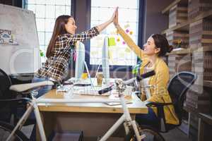 Female colleagues high fiving at computer desk
