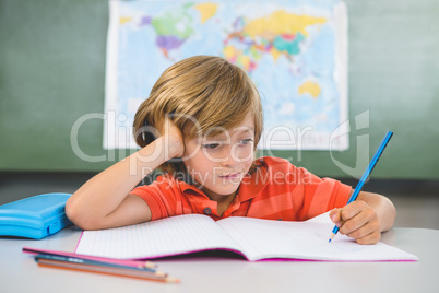 Front view of boy writing on book in classroom