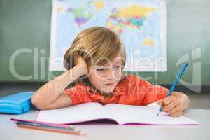 Front view of boy writing on book in classroom