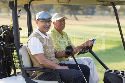 Smiling male golfer friends sitting in golf buggy