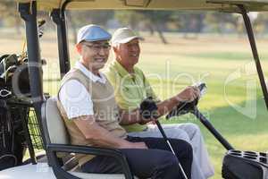 Smiling male golfer friends sitting in golf buggy