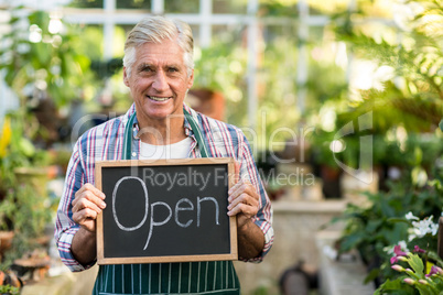 Mature owner holding open sign placard at greenhouse