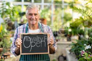 Mature owner holding open sign placard at greenhouse