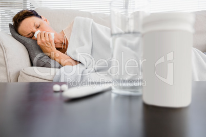 Mature woman sneezing  with medicine on foreground
