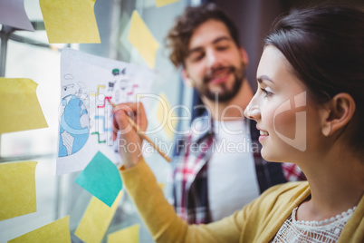 Businesswoman writing on paper stuck to glass