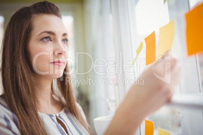 Young businesswoman looking at adhesive notes on window in creat