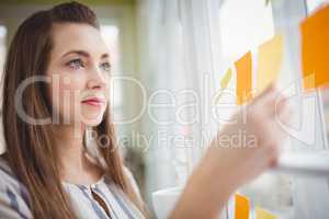 Young businesswoman looking at adhesive notes on window in creat