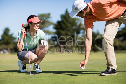 Man removing golf ball from hole by smiling woman