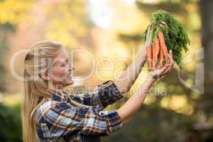 Happy female gardener holding harvested carrots