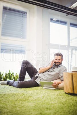 Portrait of businessman talking on phone while using laptop at c