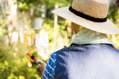 Rear view of gardener watering from hose at garden