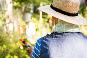 Rear view of gardener watering from hose at garden