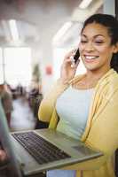 Businesswoman holding laptop while using mobile phone in cafeter