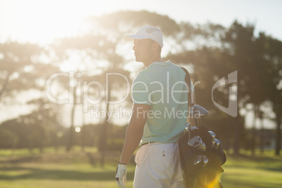 Rear view of golf player carrying bag while standing on field