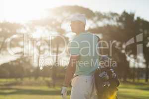 Rear view of golf player carrying bag while standing on field