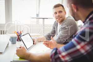 Businessmen discussing while using digital tablets in office