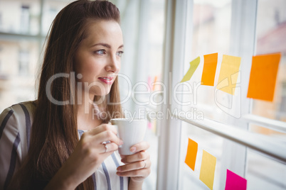 Businesswoman looking through window while having coffee in crea