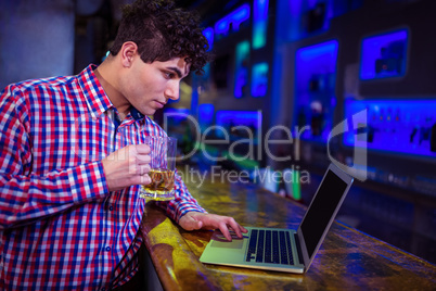Man using laptop while holding beer glass at bar counter
