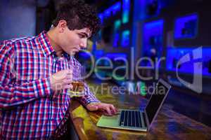 Man using laptop while holding beer glass at bar counter