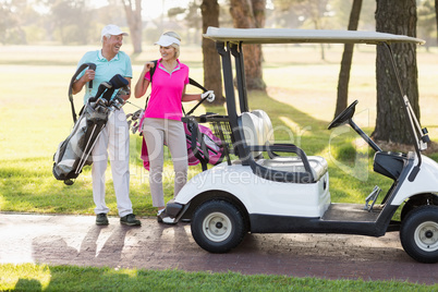 Happy mature golfer couple by golf buggy