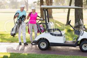 Happy mature golfer couple by golf buggy