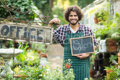 Male gardener holding open sign by office placard