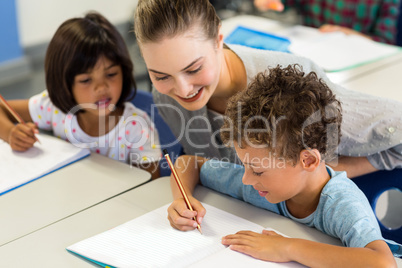 teacher helping schoolchildren to write on book