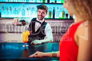 Bartender looking at woman while pouring cocktail in glass