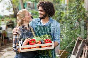 Couple holding vegetables crate outside greenhouse