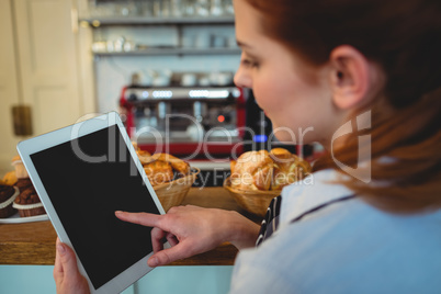 Barista scrolling digital tablet at cafe