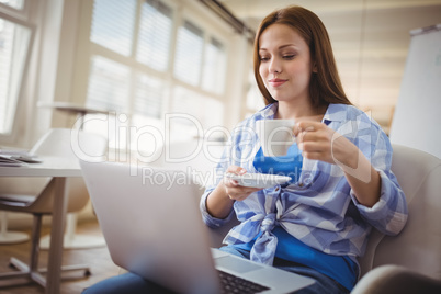 Young businesswoman having coffee while working on laptop in off