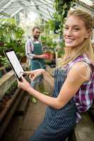 Portrait of happy gardener using digital tablet at greenhouse