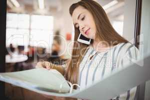Young businesswoman holding files while using mobile phone in of