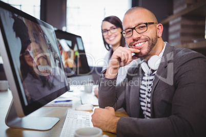 Confident businessman by computer with colleague in background