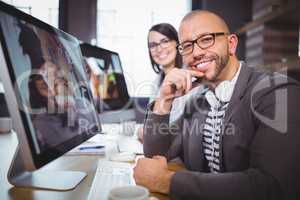 Confident businessman by computer with colleague in background