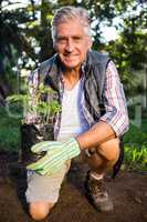 Portrait of happy gardener kneeling with potted plant at garden