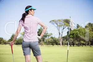 Rear view of woman holding golf club with hand on hip