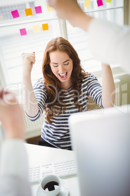 Excited businesswoman punching in air at creative office