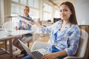 Businesswoman giving file to colleague while working on laptop a