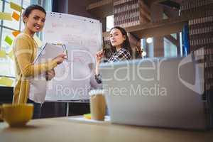 Female colleagues discussing over whiteboard