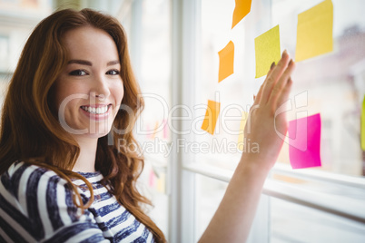 Portrait of businesswoman touching adhesive notes on window in c