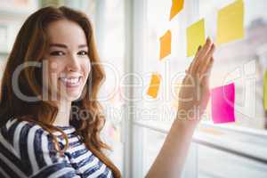 Portrait of businesswoman touching adhesive notes on window in c