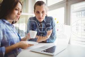 Businesswoman holding coffee cup while working with colleague