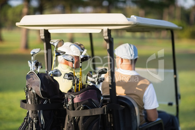 Rear view of golfer friends sitting in golf buggy