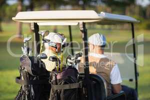 Rear view of golfer friends sitting in golf buggy