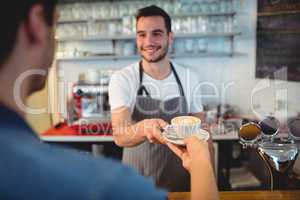 Handsome waiter serving coffee to male customer at cafeteria