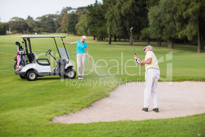 Mature golfer playing on sand trap by woman