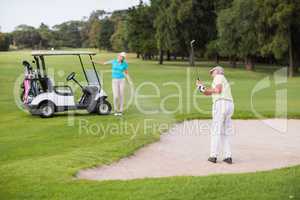 Mature golfer playing on sand trap by woman