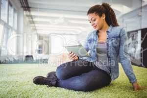 Businesswoman holding digital tablet while sitting on carpet in